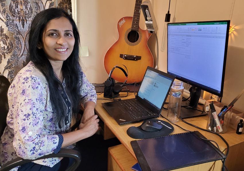 Woman in home office with computer, monitor, and guitar on her desk.