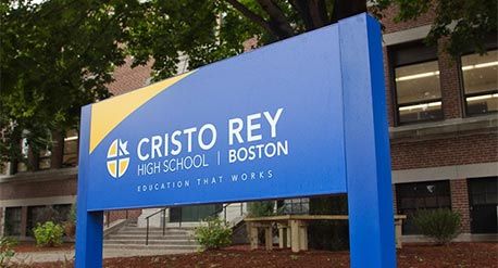 Blue sign with white lettering outside the Cristo Rey school. Sign says Cristo Rey High School, Boston – Education That Works. Image credit: Cristo Rey High School