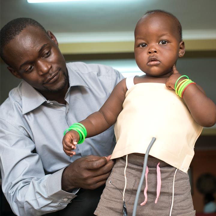 A doctor adjusts the sensor-laden Mama-Ope jacket on a child.  