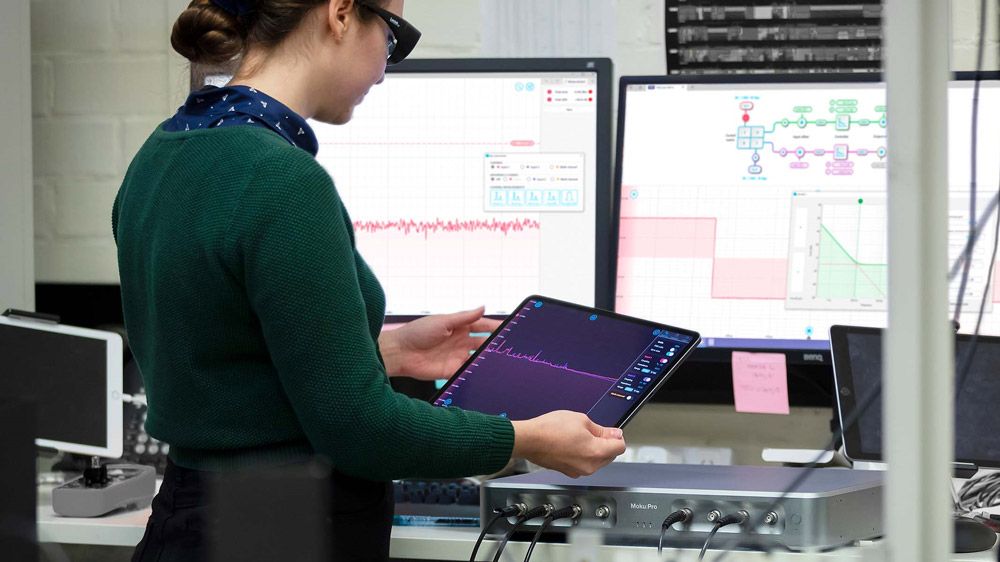 A researcher looks at Moku:Pro’s built-in instruments customized with MATLAB on a tablet and several computer screens.